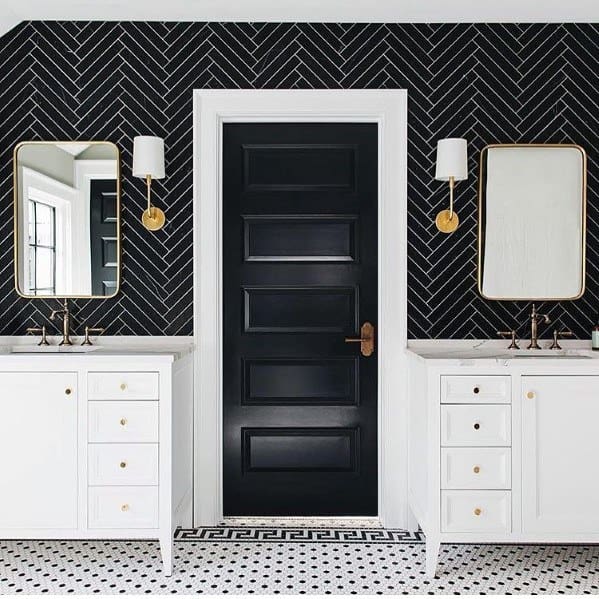 Bathroom with black beveled herringbone tile backsplash, white vanities, and gold fixtures.