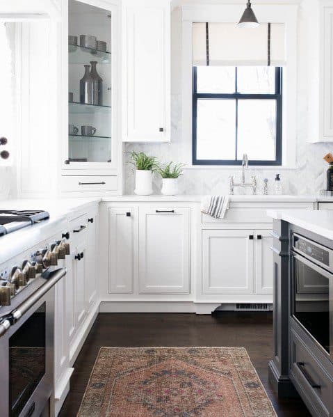 Bright kitchen with hardwood flooring, white cabinetry, a stylish rug, and modern appliances, complemented by natural light