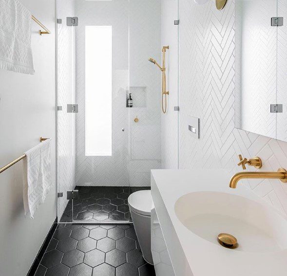 Small modern bathroom with white herringbone tiles, black hexagon flooring, and gold fixtures.