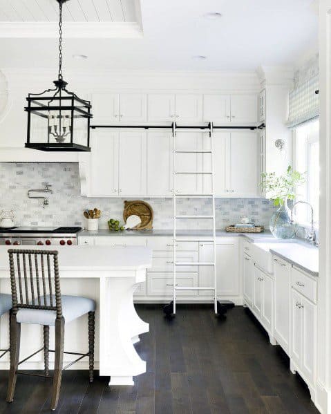 Bright kitchen with dark brown hardwood flooring, white cabinetry, a unique ladder for upper shelves, and modern light fixtures