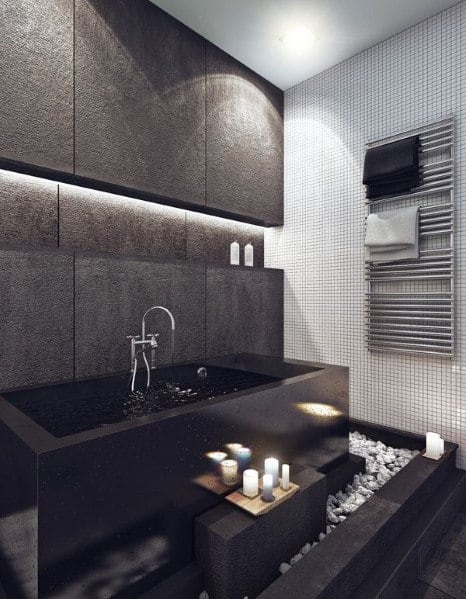 Modern bathroom with black stone bathtub, candles, and white pebble flooring accents.