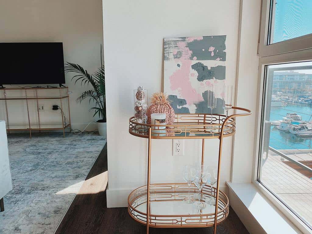 Gold circular bar cart with decorative accents, champagne flutes, and abstract wall art nearby.