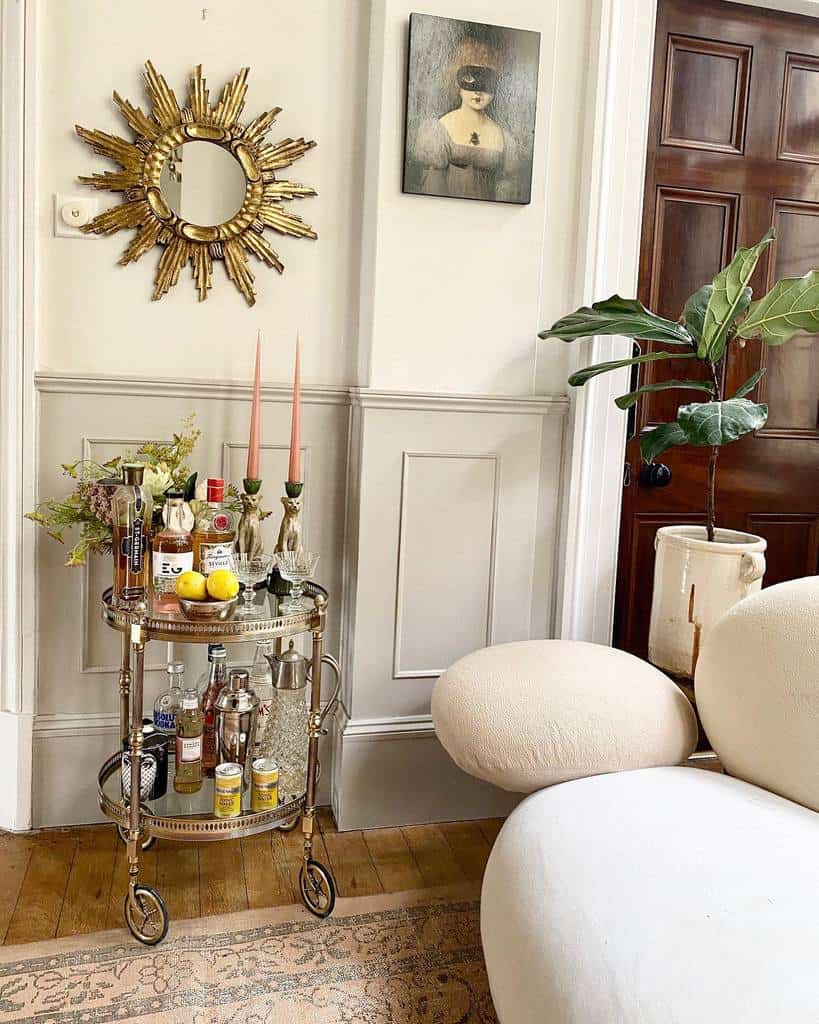 Vintage bar cart with assorted liquors, candles, and decorative accents under a sunburst mirror.