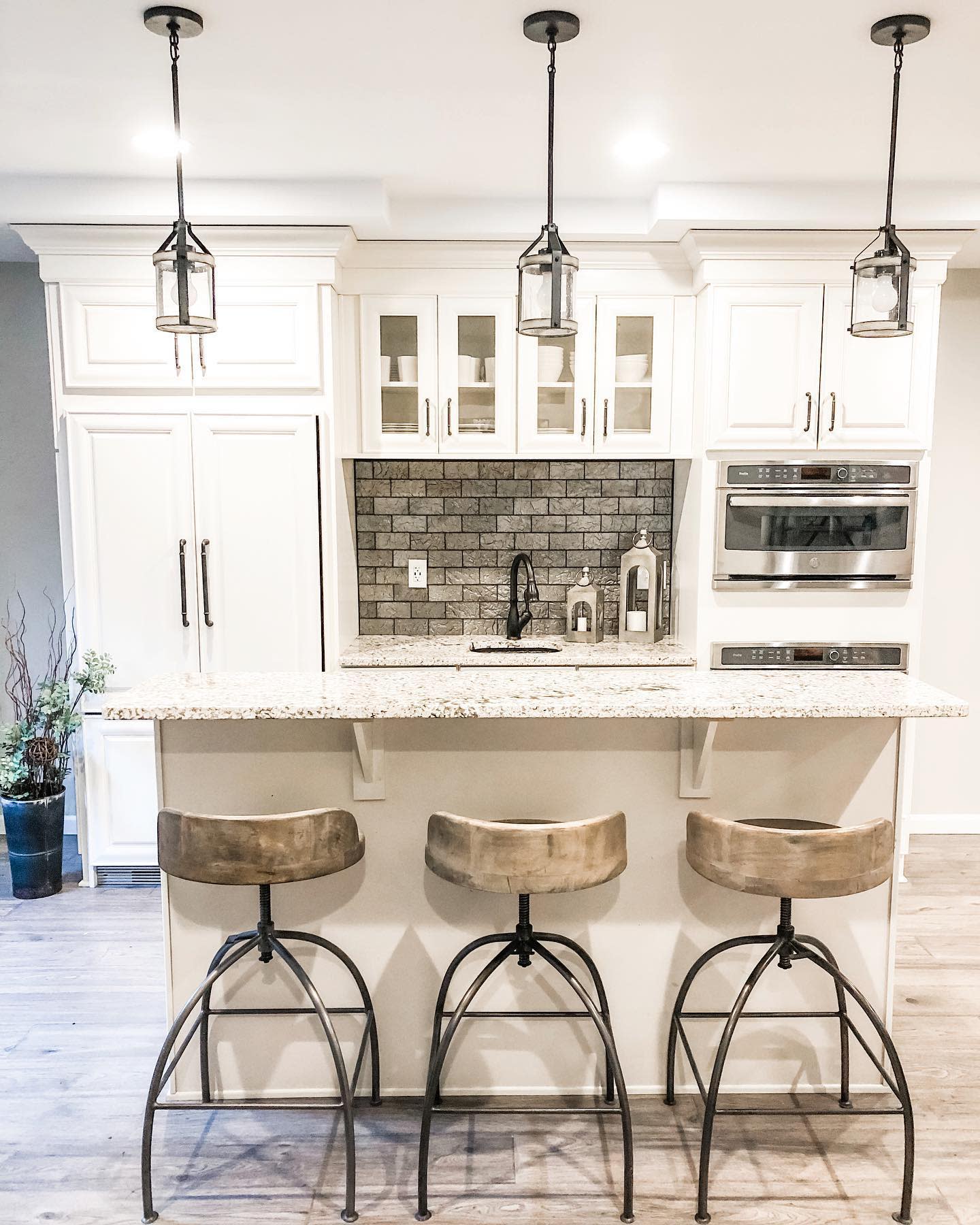 Modern white kitchen with marble countertops, brick backsplash, and industrial bar stools.