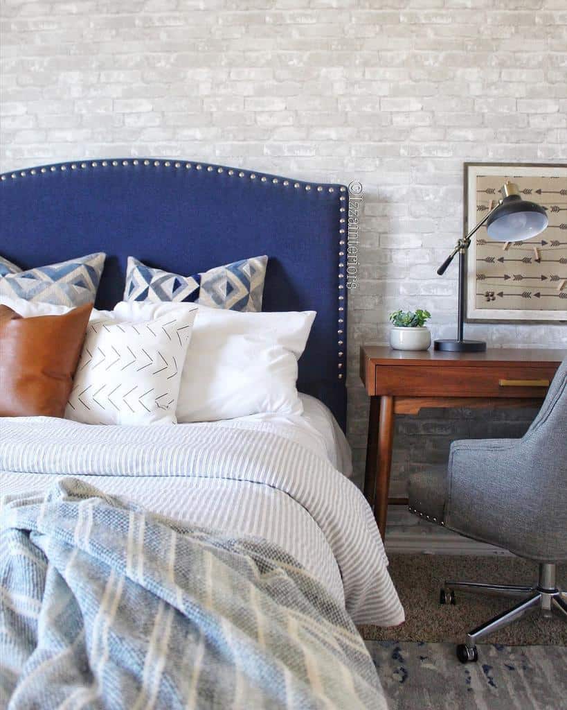 Bedroom with white brick wallpaper, blue upholstered bed, wooden desk, and modern lamp.