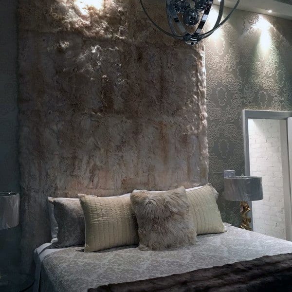 Bedroom with a faux fur accent wall, patterned wallpaper, and soft textured bedding.