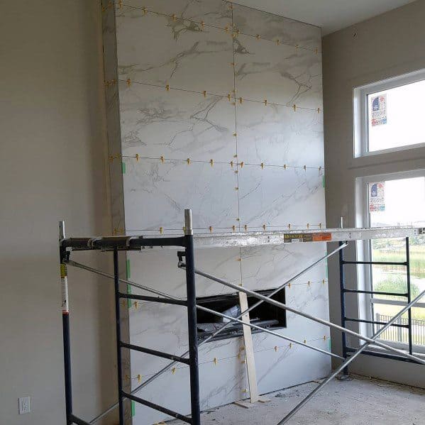 Large floor-to-ceiling fireplace with white marble tiles and scaffolding for installation.