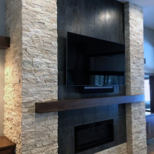 A modern fireplace with dark sleek tiles, light stone columns, and a wooden mantle under a built-in TV.