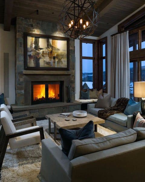 Cozy living room with a stone fireplace, modern art, plush seating, and a large window view of a winter landscape