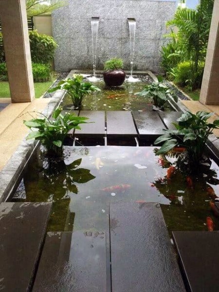 Dual waterfall feature flowing into a koi pond with floating platforms and surrounded by tropical plants.