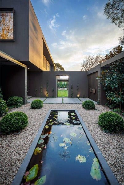 Modern courtyard pond with water lilies, surrounded by gravel paths and manicured greenery.