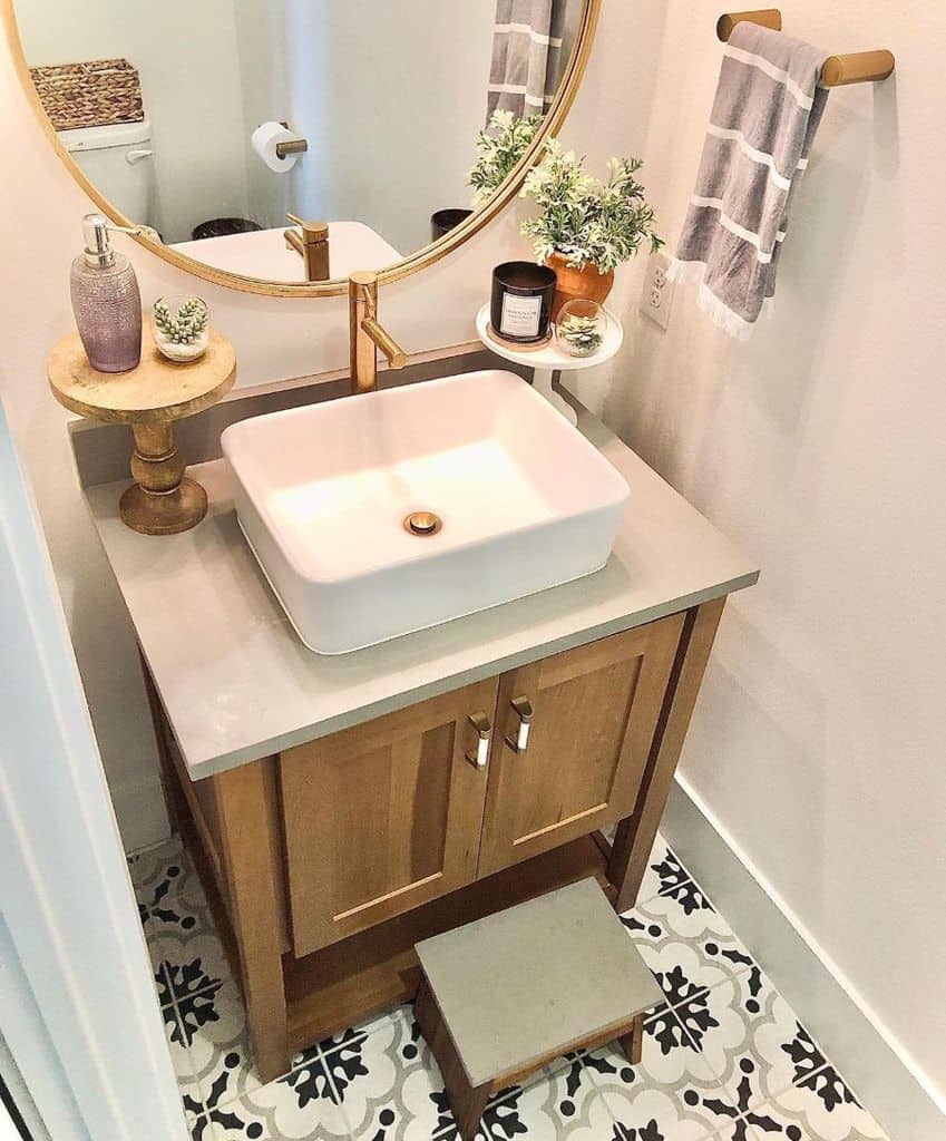 Small bathroom with vessel sink, gold accents, round mirror, and patterned tile floor.