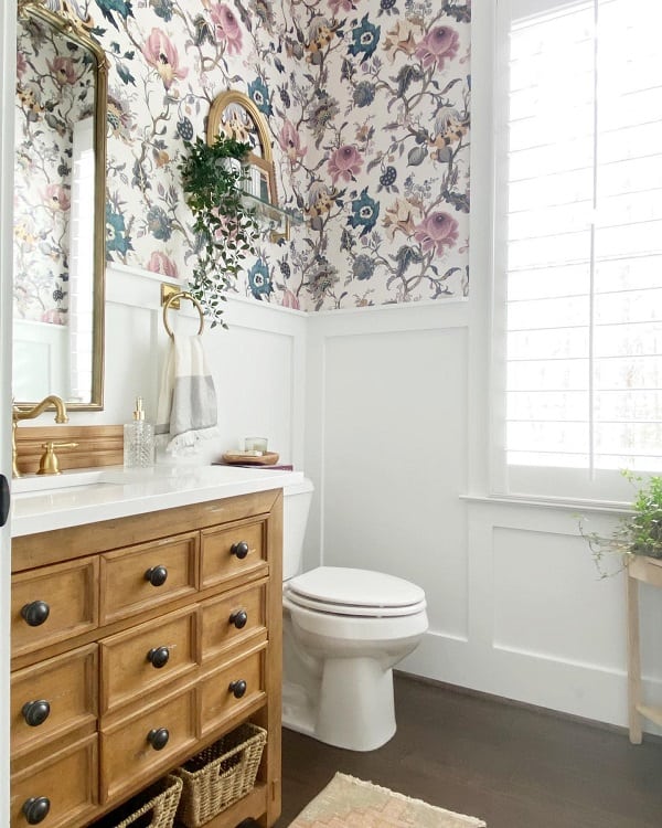 Bathroom with floral wallpaper, wood vanity, and white wainscoting.