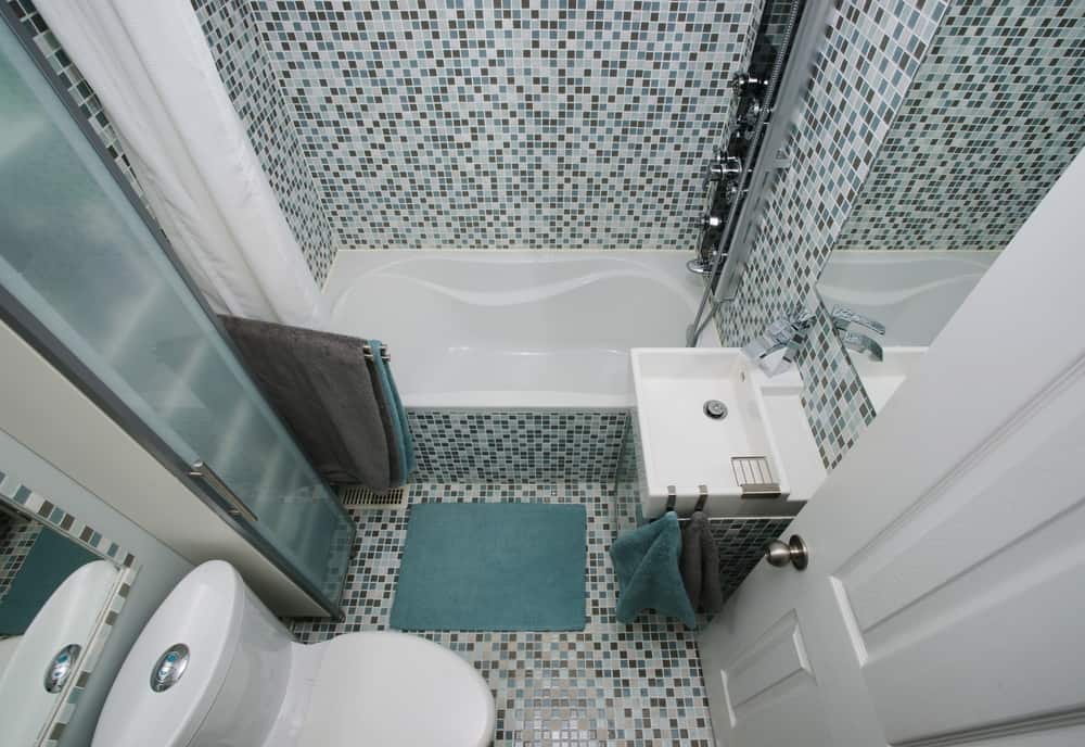 Small bathroom with blue and gray mosaic wall tiles, bathtub, and compact sink.