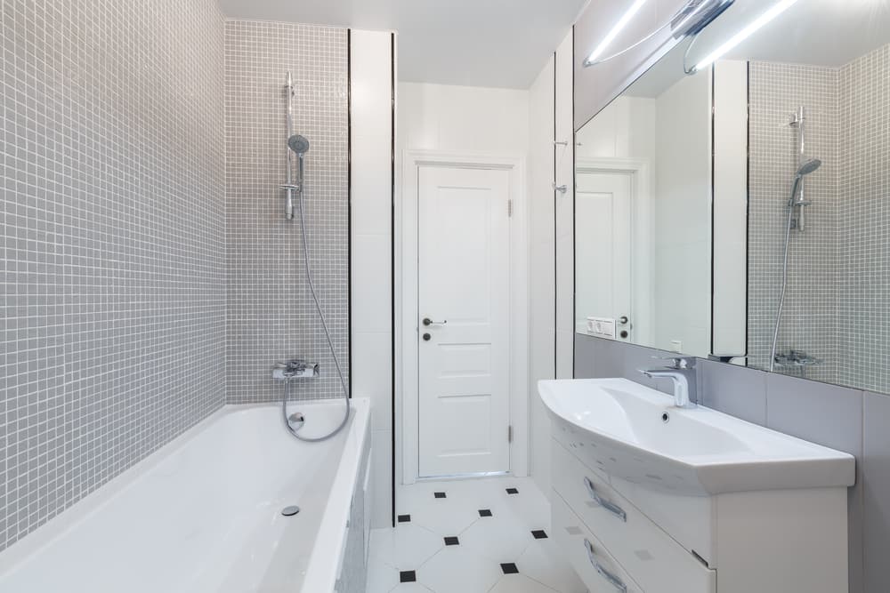 Bathroom with white bathtub, mosaic tile wall, large mirror, and modern sink.