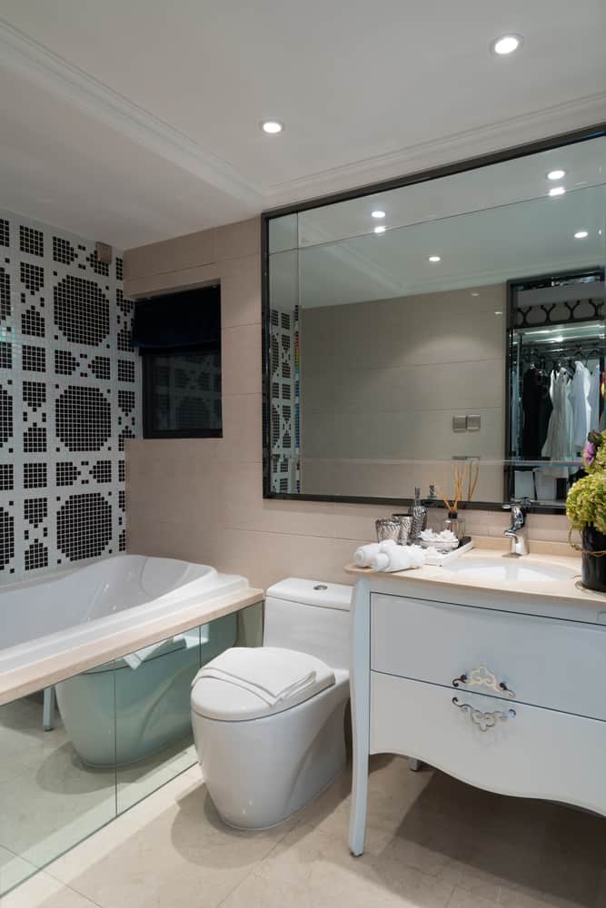 Modern bathroom with white fixtures, large mirror, and decorative tiled wall next to the bathtub