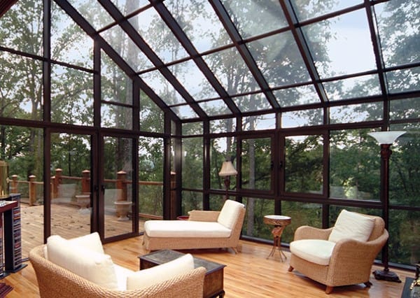 A sunroom with a glass ceiling, floor-to-ceiling windows, and wicker chaise lounges.