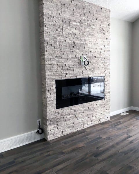 A sleek modern fireplace surrounded by textured full-wall beige stacked stone tiles for a minimalist design.