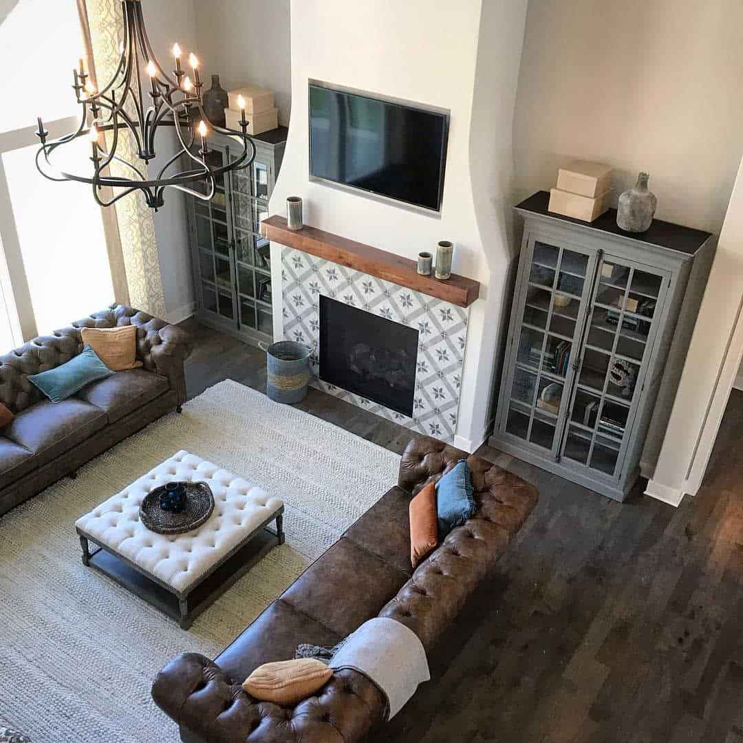 Elegant living room with brown leather sofas, a fireplace with decorative tiles, a chandelier, and a mounted TV