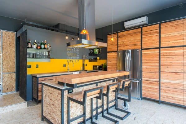 Modern garage bar with wooden accents, industrial stools, yellow backsplash, and open shelving.