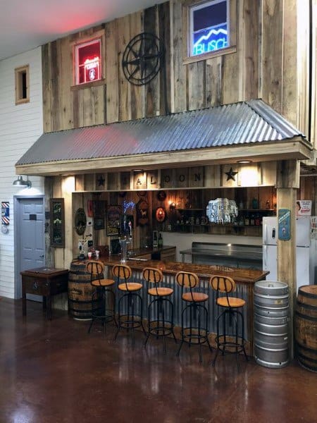 Rustic saloon-style garage bar with wooden decor, barrel accents, and metal bar stools.