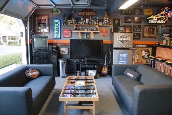 Garage lounge with Harley-Davidson decor, neon signs, comfy seating, and entertainment setup.