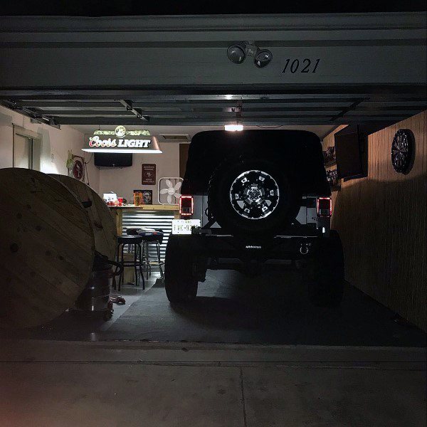 Garage bar with a parked Jeep, Coors Light sign, corrugated metal counter, and casual seating.