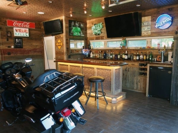 Motorcycle-themed garage bar with rustic wood decor, neon signs, and mounted TVs.