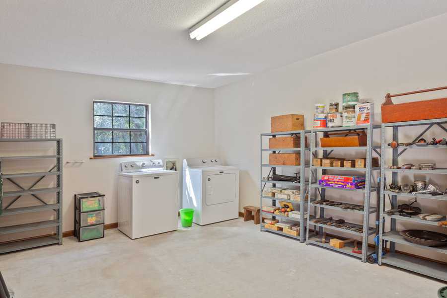 Interior of a large garage shed with a washing machine, dryer, and metal shelving units holding tools and supplies.