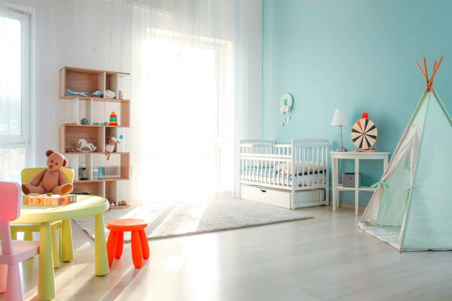 Bright baby room with crib, play tent, colorful table, and wooden storage shelf.