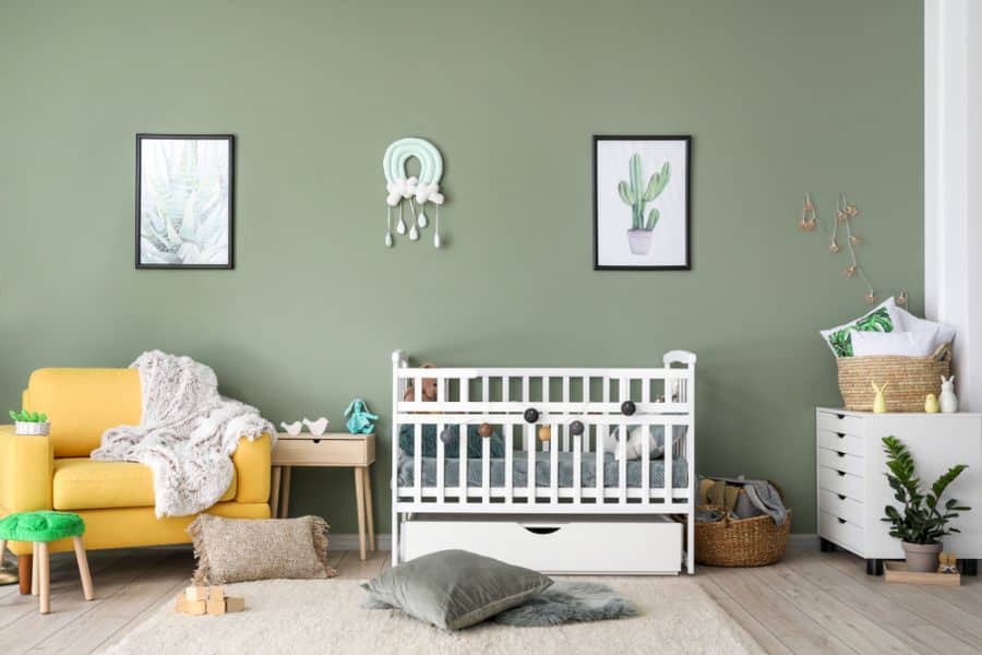 Modern baby room with green walls, white crib, yellow armchair, and natural decor accents.