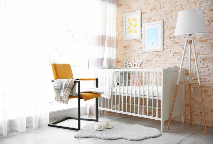 Modern baby room with crib, yellow chair, floor lamp, and decorative wall art.