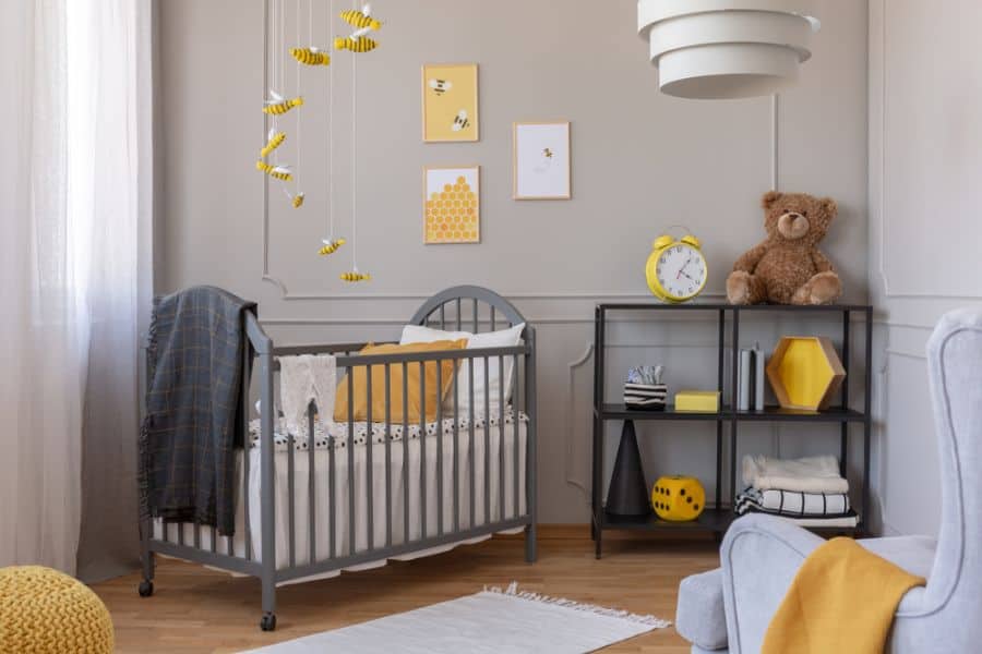 Gray and yellow baby room with crib, shelf, teddy bear, and bee-themed decor.