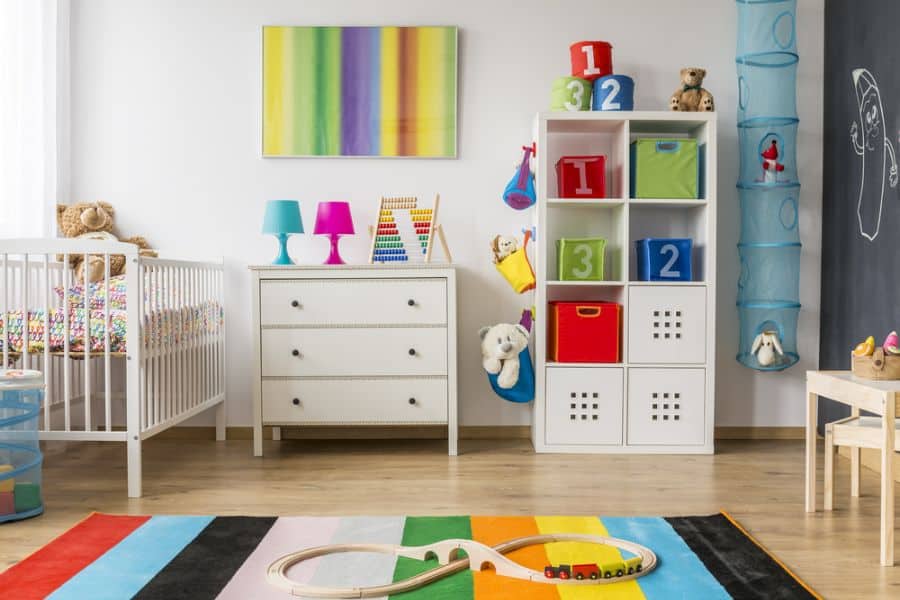 Colorful baby room with crib, dresser, rainbow rug, toy storage, and playful wall decor.