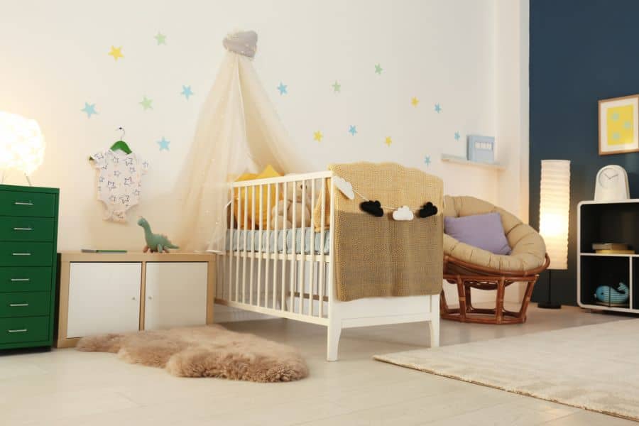 Neutral baby room with crib, star wall decals, cozy chair, and green dresser.