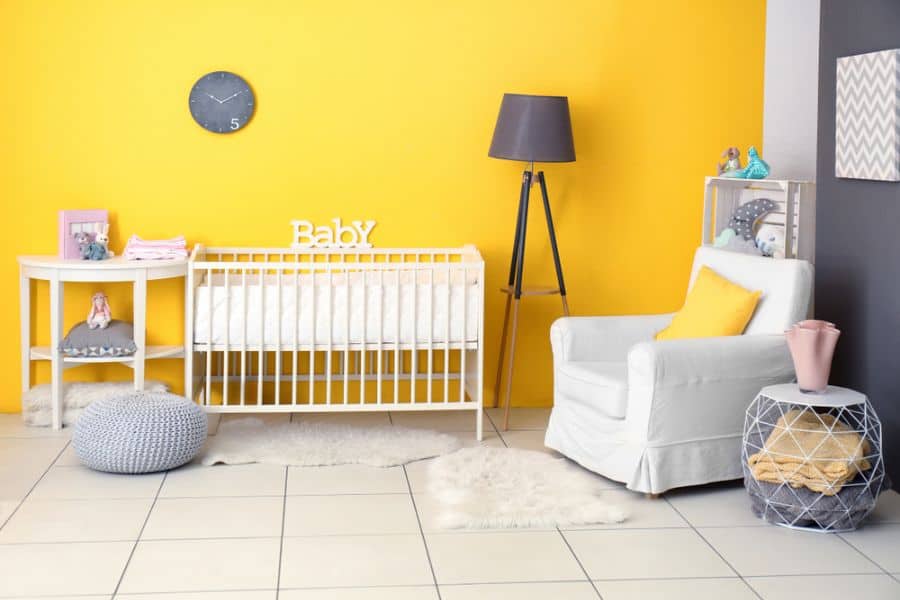 Baby room with yellow feature wall, white crib, armchair, and modern decor accents.