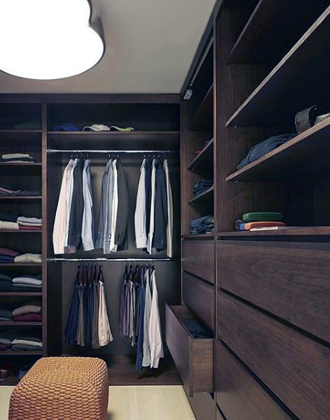 A neatly organized walk-in closet with hanging shirts, folded clothes on shelves, and a woven ottoman on the floor