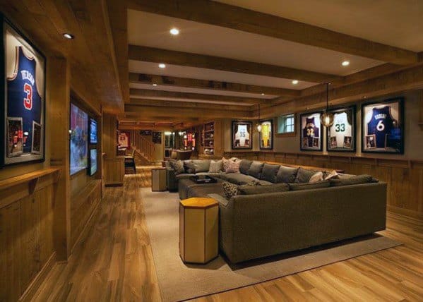 Cozy mancave with wood accents, spacious sectional sofa, framed sports jerseys, and warm lighting.