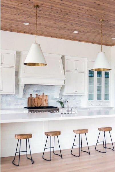 Stylish kitchen featuring large white dome pendant lights above a minimalist island with wooden bar stools and a warm wood ceiling