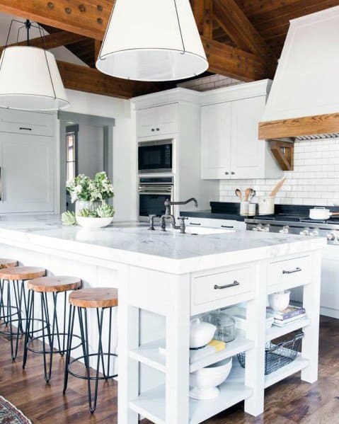 Bright kitchen featuring large white pendant lights above a marble island, with wooden stools and exposed wooden beams