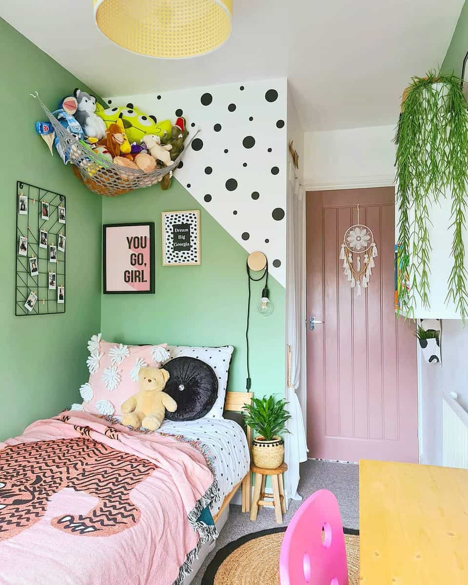 A colorful bedroom with green and polka-dot walls, a pink door, and a bed with stuffed animals and a "You Go, Girl" poster