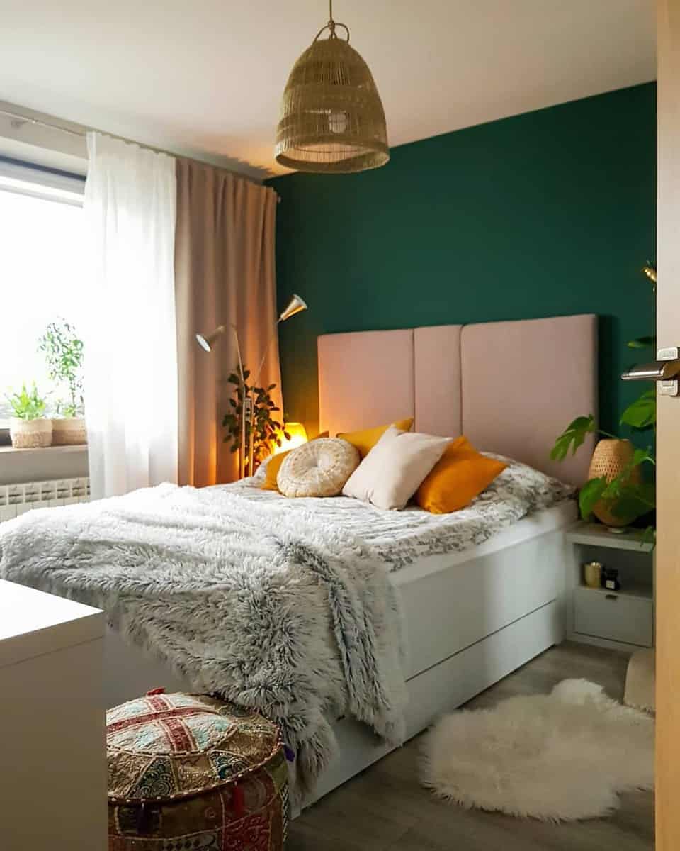 Cozy bedroom with green accent wall, bed with gray and orange pillows, and plants by the window