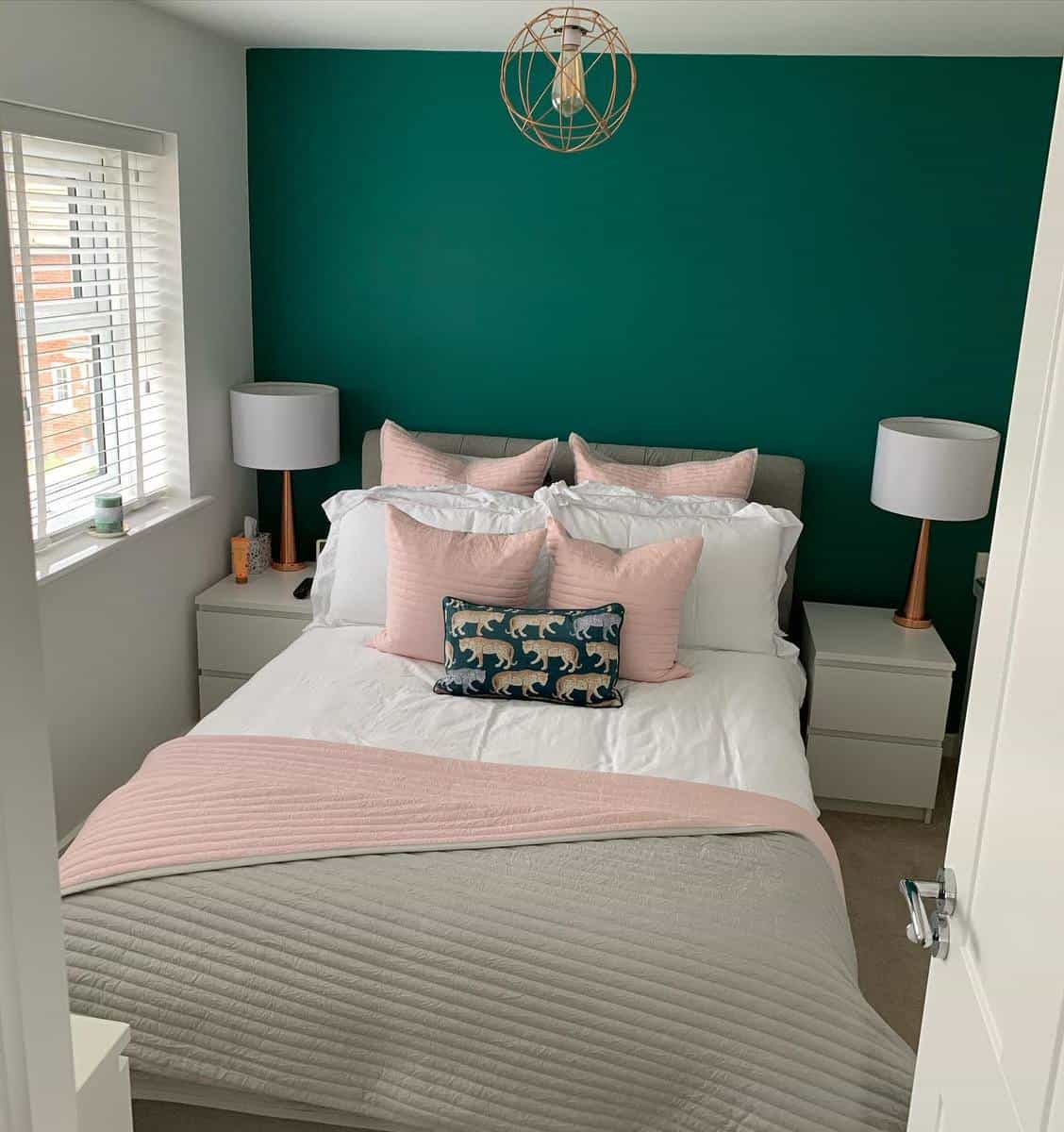 Cozy bedroom with teal accent wall, pink pillows and throw, and two bedside lamps on white nightstands