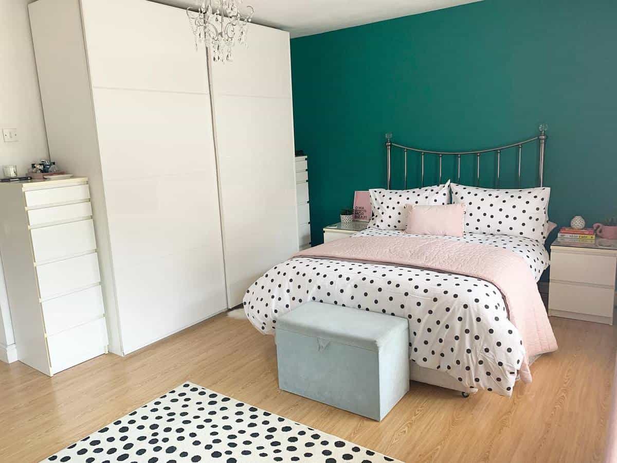 Bedroom with a teal accent wall, polka dot bedding, white furniture, and a chandelier