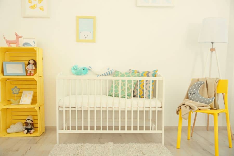 Cheerful baby room with yellow accents, white crib, and colorful pillows.