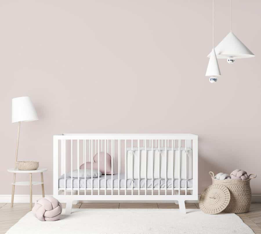 Minimalist nursery with white crib, soft pink pillows, and modern pendant lights.