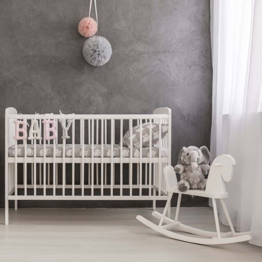 Modern baby room with gray accent wall, white crib, and rocking horse with plush toy.