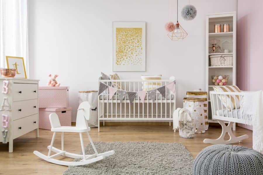 Chic baby girl's room with white crib, rocking horse, and pastel decor accents.