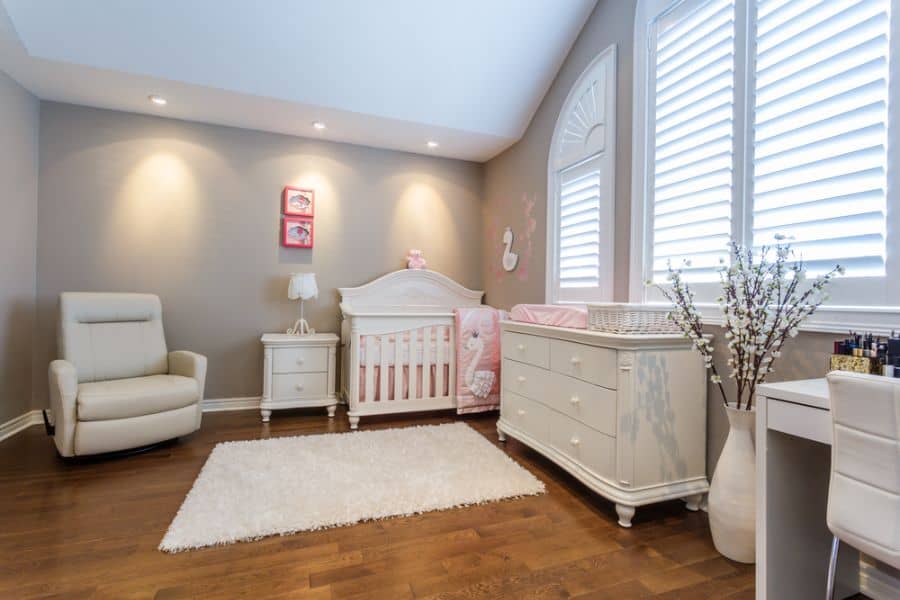 Elegant baby girl's room with white crib, soft lighting, and cozy seating area.