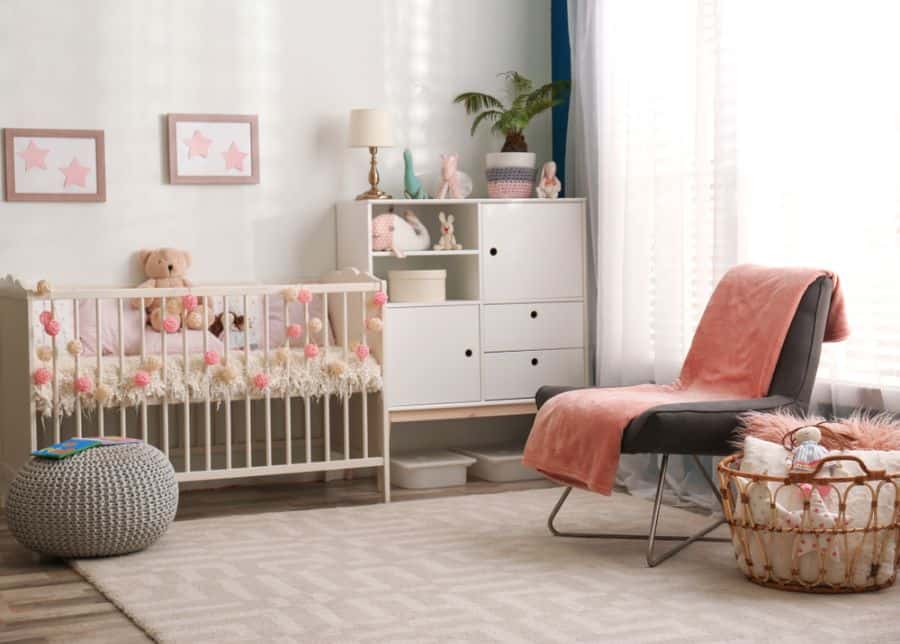 Spacious baby girl's room with pink accents, cozy chair, and decorative crib details.